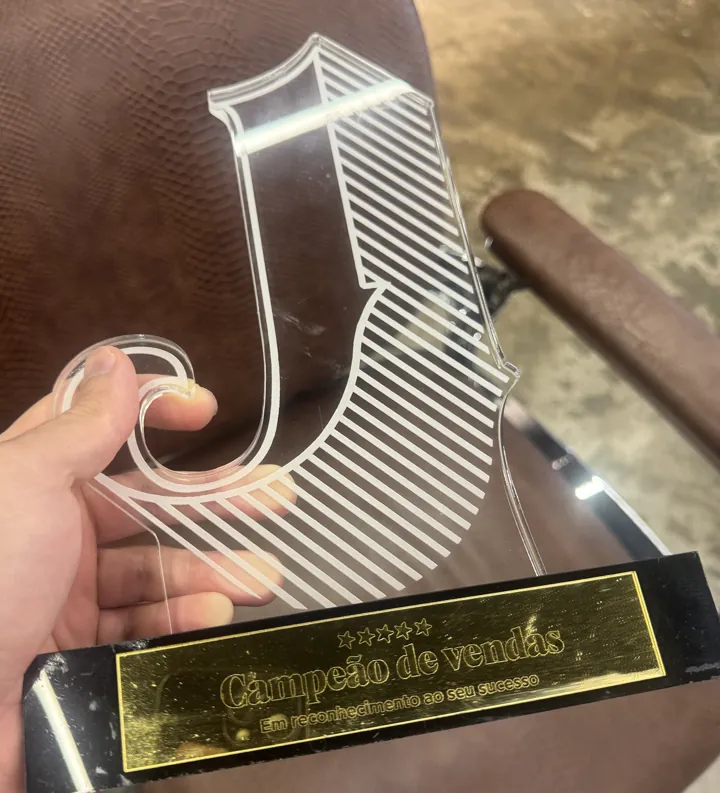 Troféu de acrílico com a letra J e a placa dourada "Campeão de vendas — Em reconhecimento ao seu sucesso"